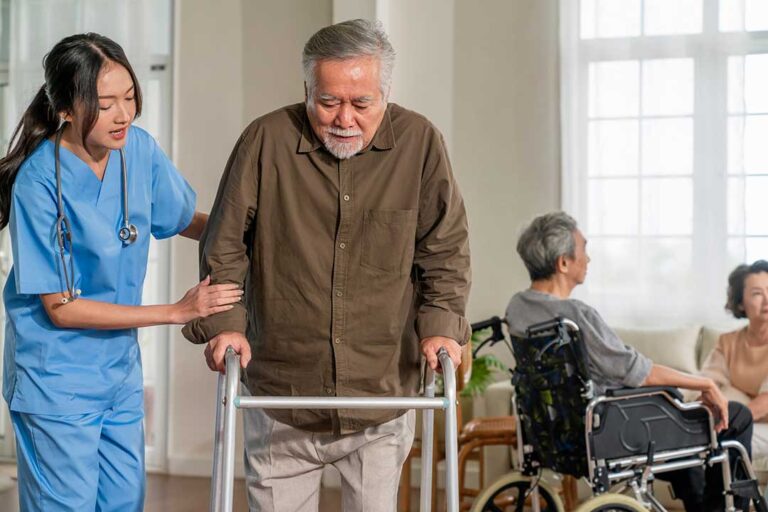 Senior woman using a walker with grab bars and non-slip mats visible in a well-lit hallway.