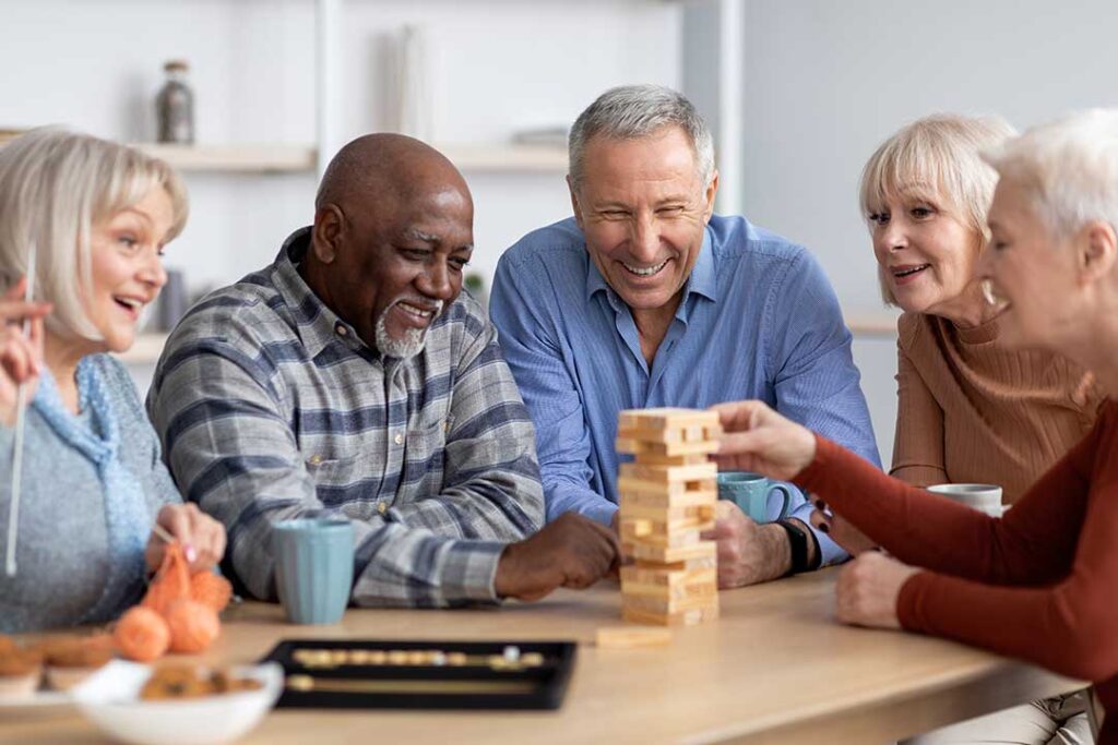 Older adults seated together making seasonal crafts near a bright window with plants and colorful decorations.